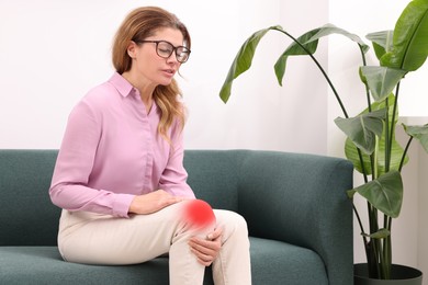 Image of Woman suffering from pain in knee on sofa indoors