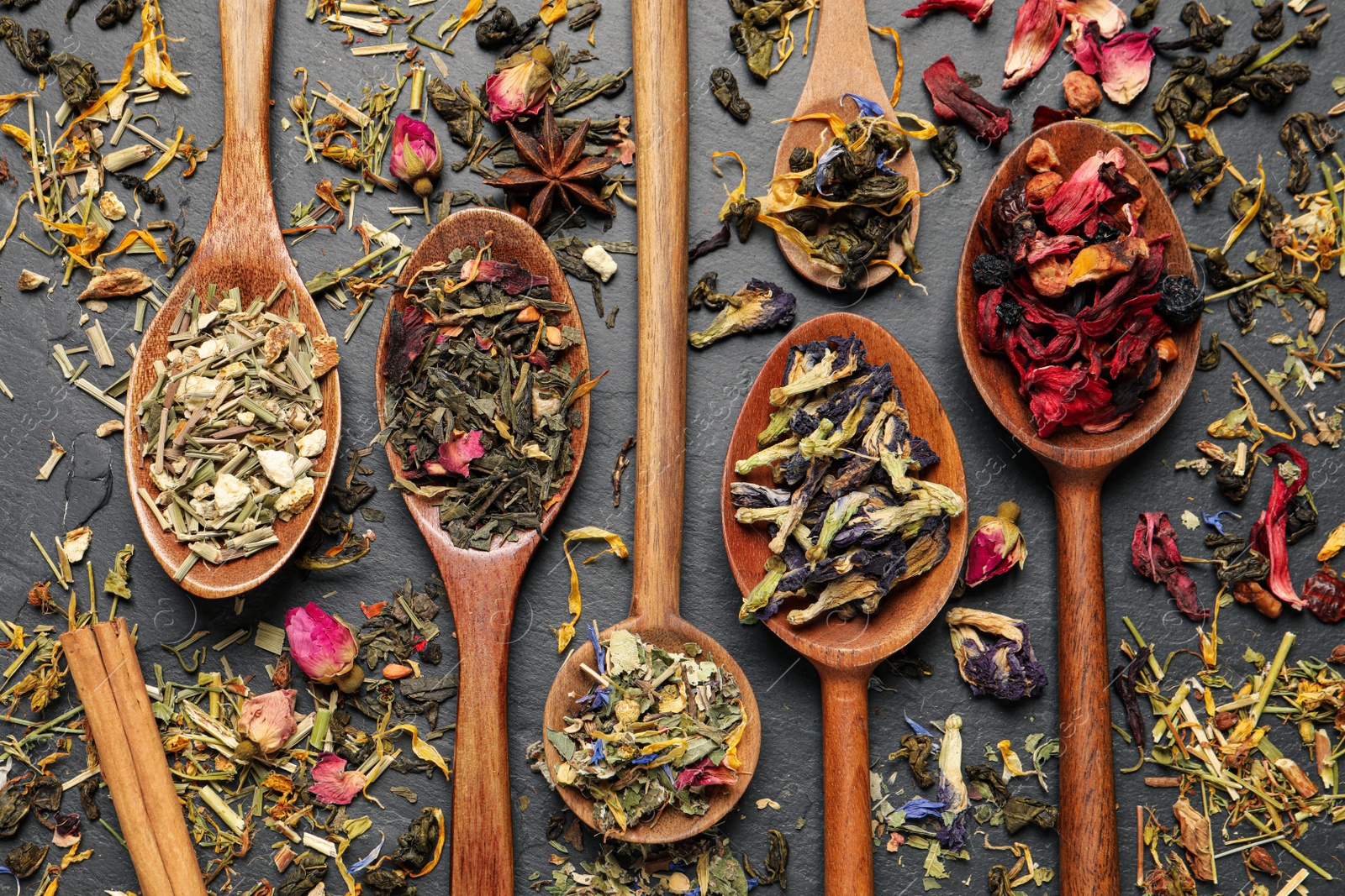 Photo of Wooden spoons with different teas on black table, flat lay