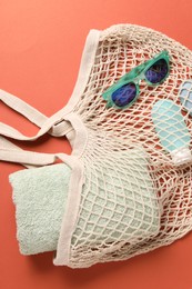 Photo of String bag, sunglasses, cosmetic product and towel on coral background, top view