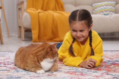 Smiling little girl and cute ginger cat on carpet at home