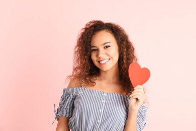 African-American woman with paper heart on color background