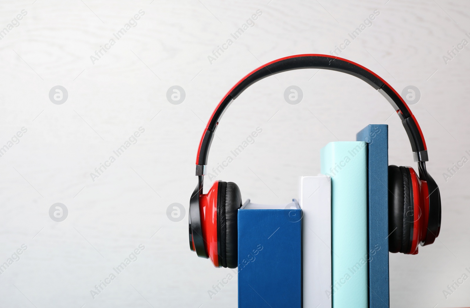 Photo of Modern headphones with hardcover books on light background, closeup. Space for text