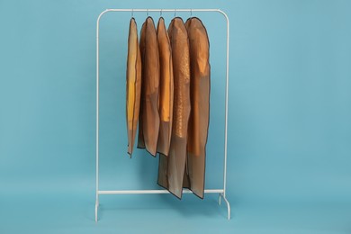 Photo of Garment bags with clothes on rack against light blue background