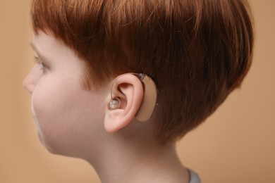 Little boy with hearing aid on pale brown background, closeup