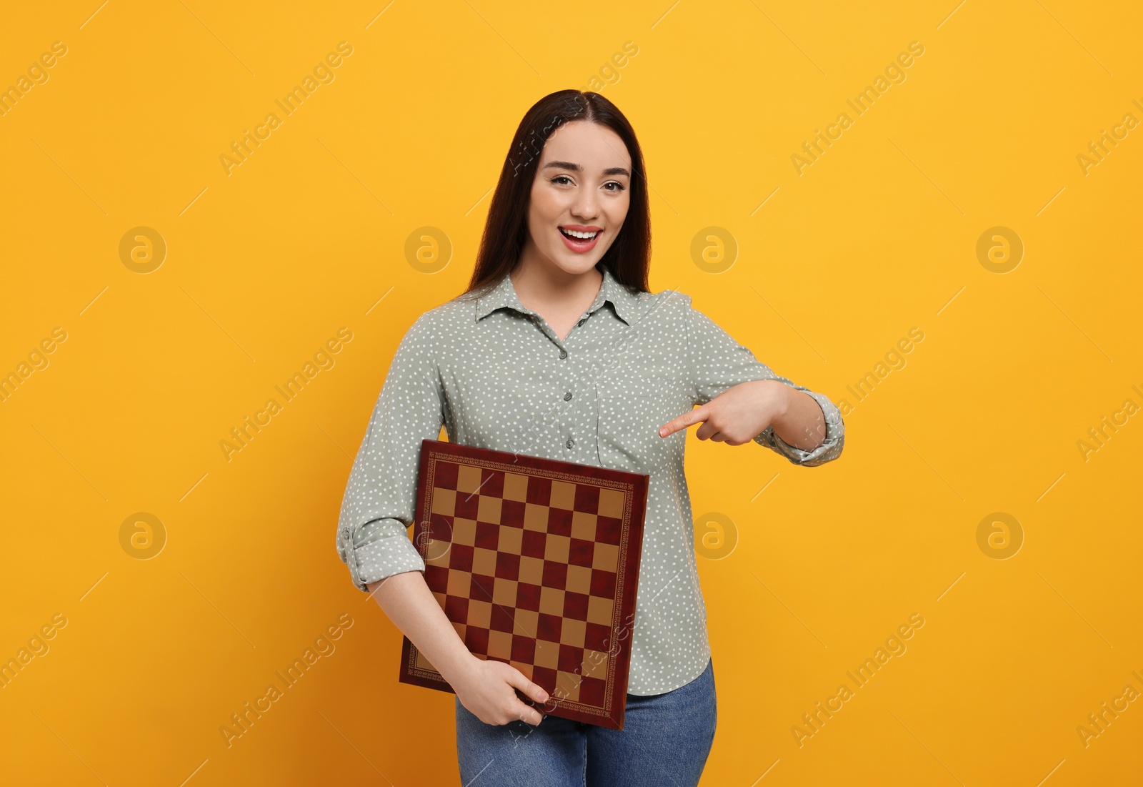 Photo of Happy woman showing chessboard on orange background