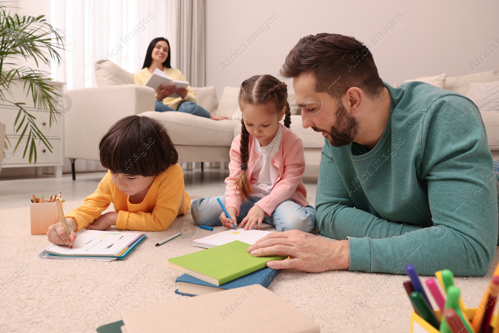 Photo of Father playing with his children while mother reading book on sofa in living room