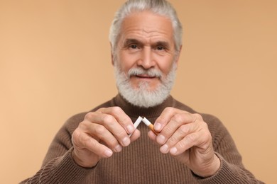Photo of Stop smoking concept. Senior man breaking cigarette on beige background, selective focus