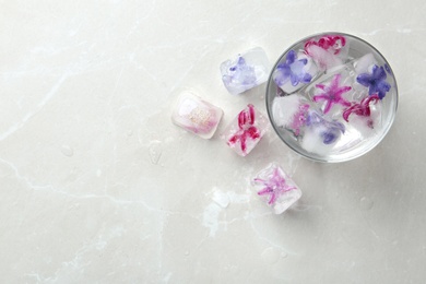 Photo of Glass of water and ice cubes with flowers on table, top view. Space for text