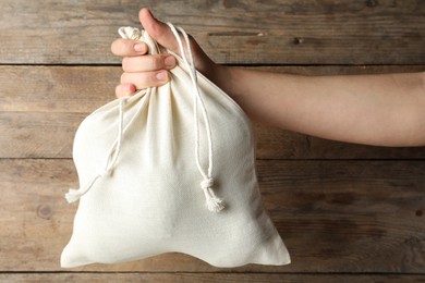 Photo of Woman holding full cotton eco bag on wooden background, closeup