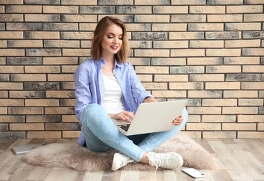 Photo of Beautiful young woman using laptop while sitting on floor near brick wall