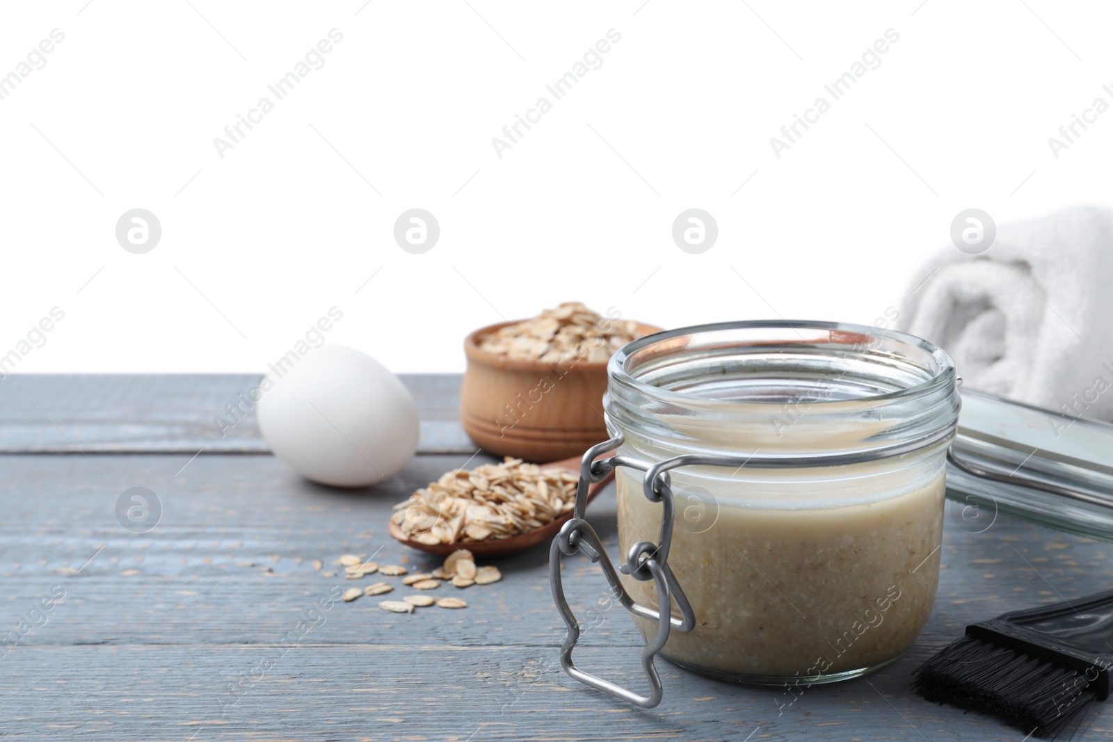 Photo of Homemade hair mask in jar, fresh ingredients and brush on grey wooden table against white background. Space for text