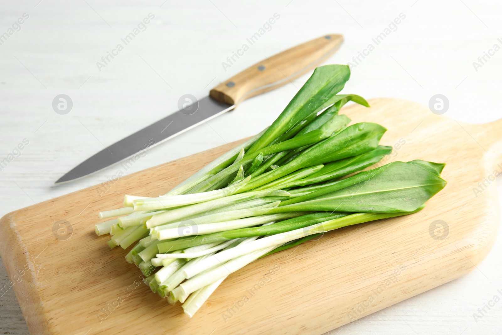 Photo of Board with wild garlic or ramson and knife on white wooden table, closeup