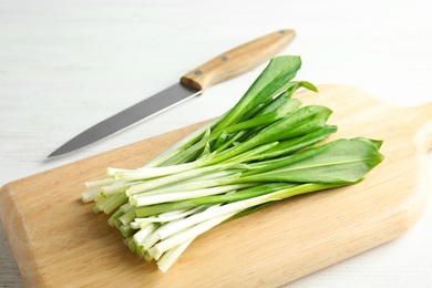 Board with wild garlic or ramson and knife on white wooden table, closeup