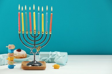 Hanukkah celebration. Menorah with burning candles, dreidels, donut and gift boxes on white wooden table against light blue background. Space for text