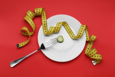 Photo of Plate with cucumber slice, measuring tape and fork on red background, top view. Diet concept