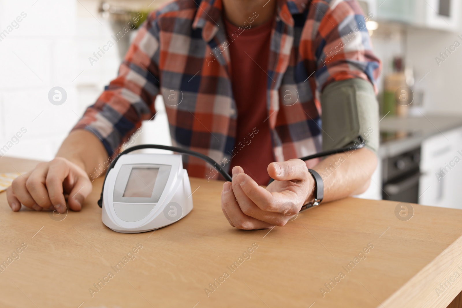 Photo of Man checking blood pressure with sphygmomanometer at table indoors, closeup. Cardiology concept