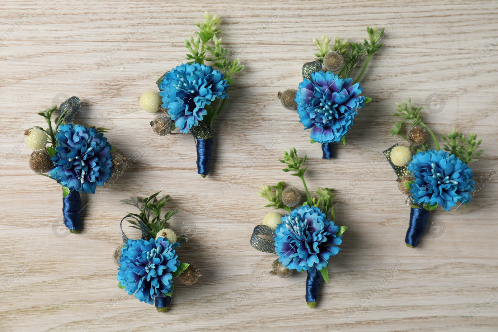 Photo of Stylish blue boutonnieres on white wooden table, flat lay