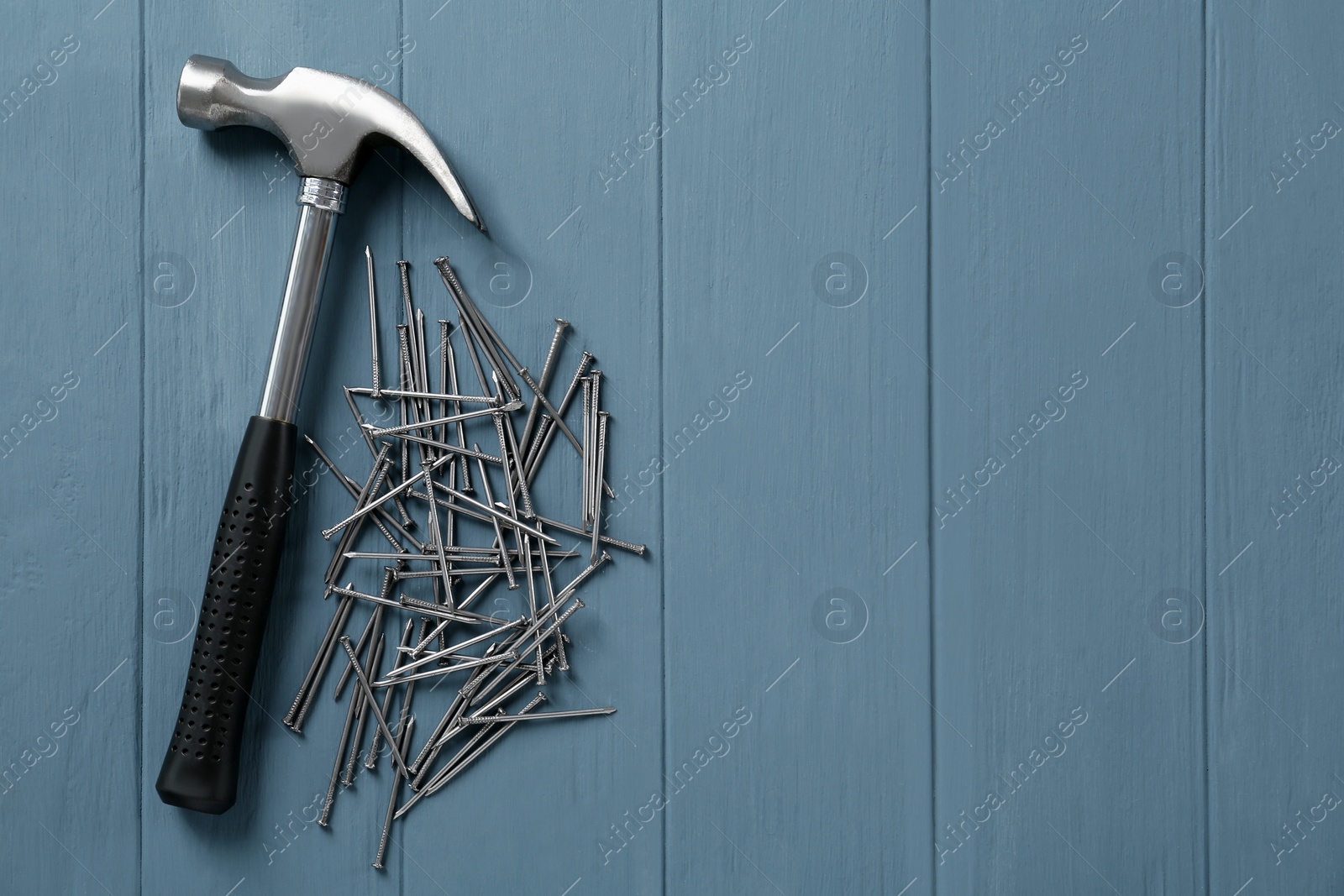 Photo of Hammer and metal nails on light blue wooden table, flat lay. Space for text