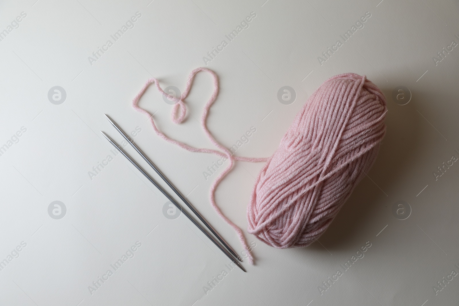 Photo of Soft pink yarn and metal knitting needles on light background, top view