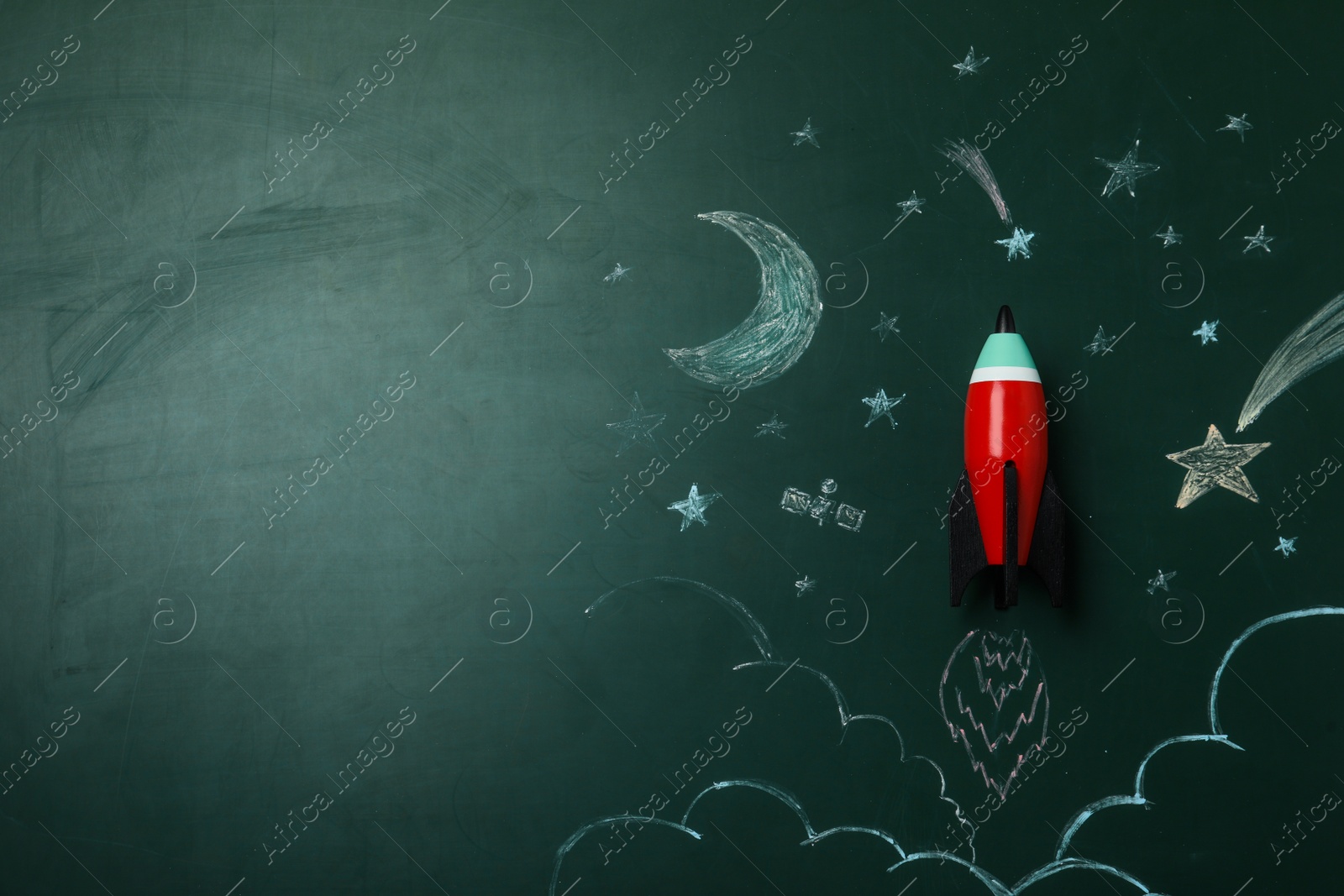 Photo of Bright toy rocket and drawings on chalkboard, top view. Space for text