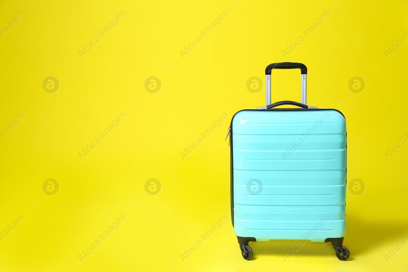 Photo of Stylish blue suitcase on yellow background. Space for text