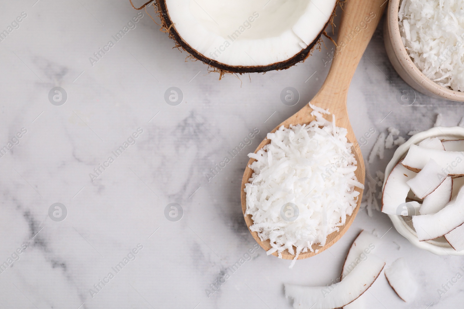 Photo of Coconut flakes, nut and spoon on white marble table, flat lay. Space for text
