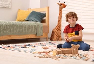 Little boy playing with wooden construction set on carpet in room, space for text. Child's toy