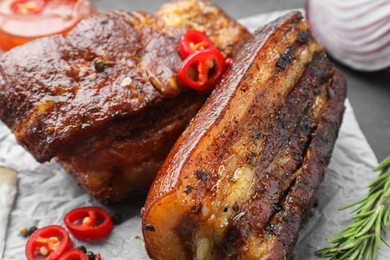 Pieces of baked pork belly served with rosemary and chili pepper on table, closeup