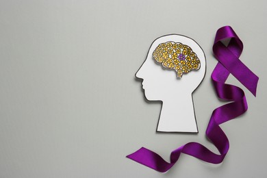 Human head cutout, brain and purple ribbon on light grey background, flat lay with space for text. Epilepsy awareness