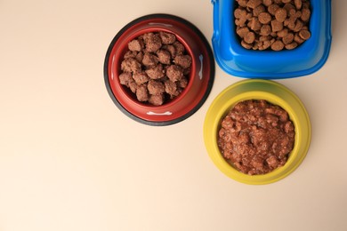 Photo of Dry and wet pet food in feeding bowls on beige background, flat lay. Space for text