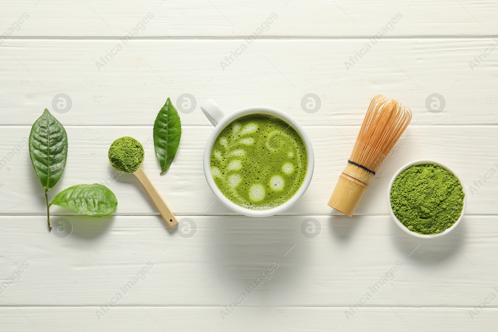 Photo of Delicious matcha latte, powder, leaves and whisk on white wooden table, flat lay