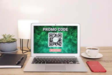 Photo of Laptop with activated promo code on wooden table indoors
