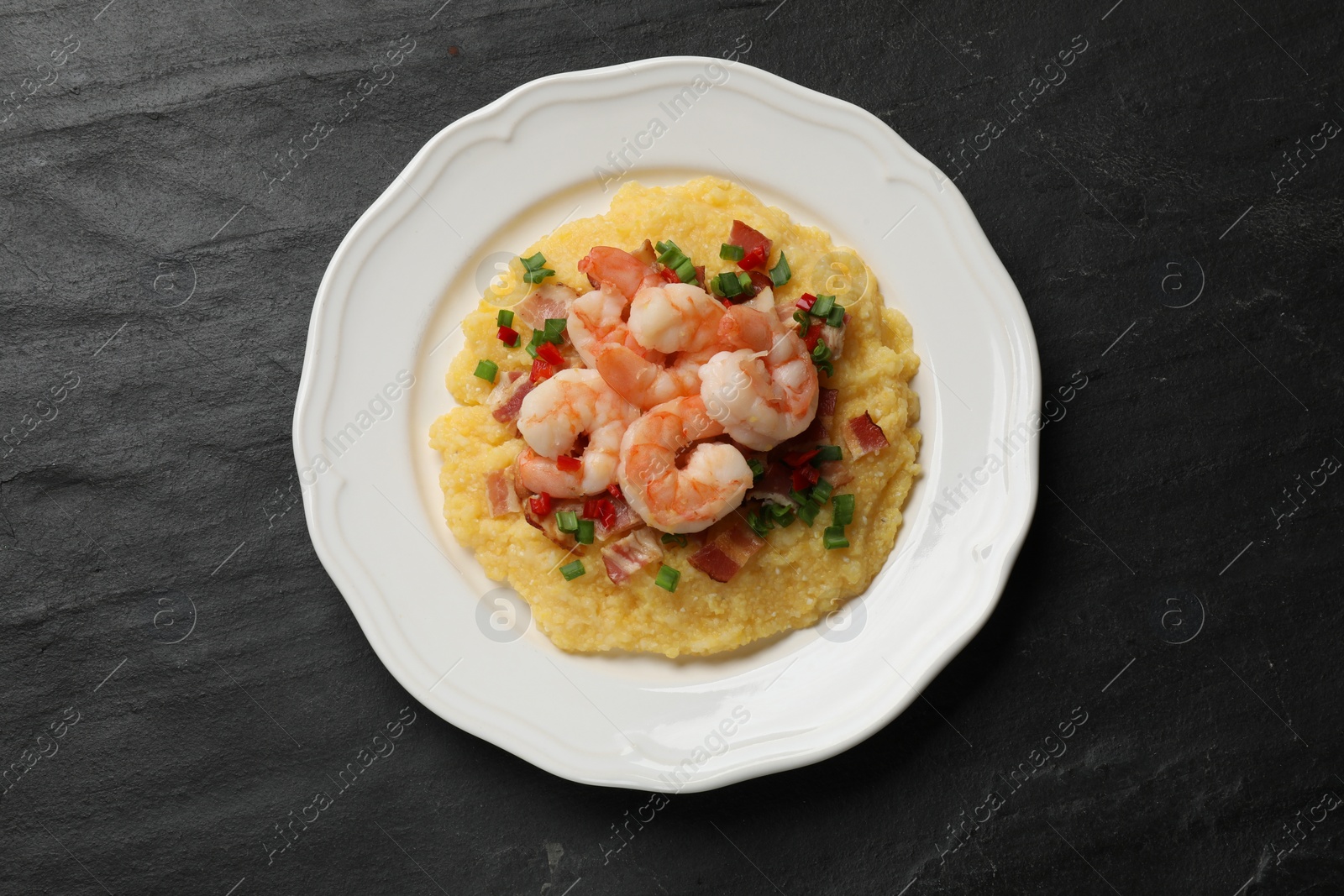 Photo of Plate with fresh tasty shrimps, bacon, grits, green onion and pepper on black textured table, top view