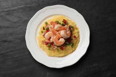 Photo of Plate with fresh tasty shrimps, bacon, grits, green onion and pepper on black textured table, top view