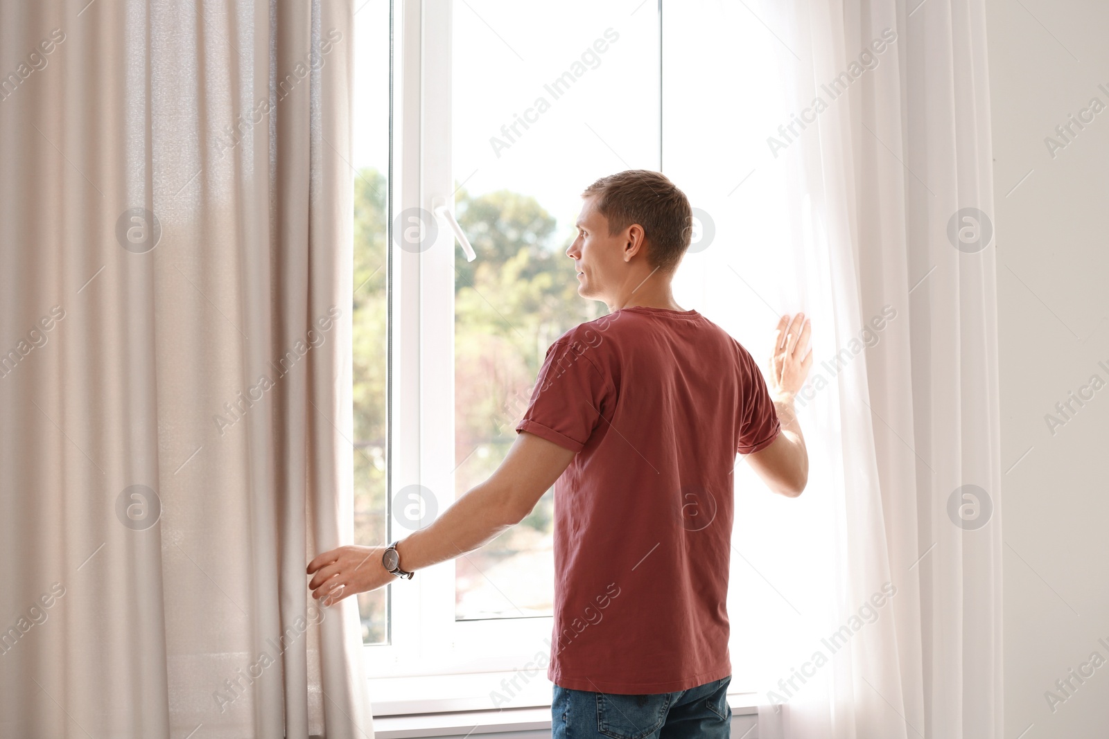Photo of Mature man opening window curtains at home