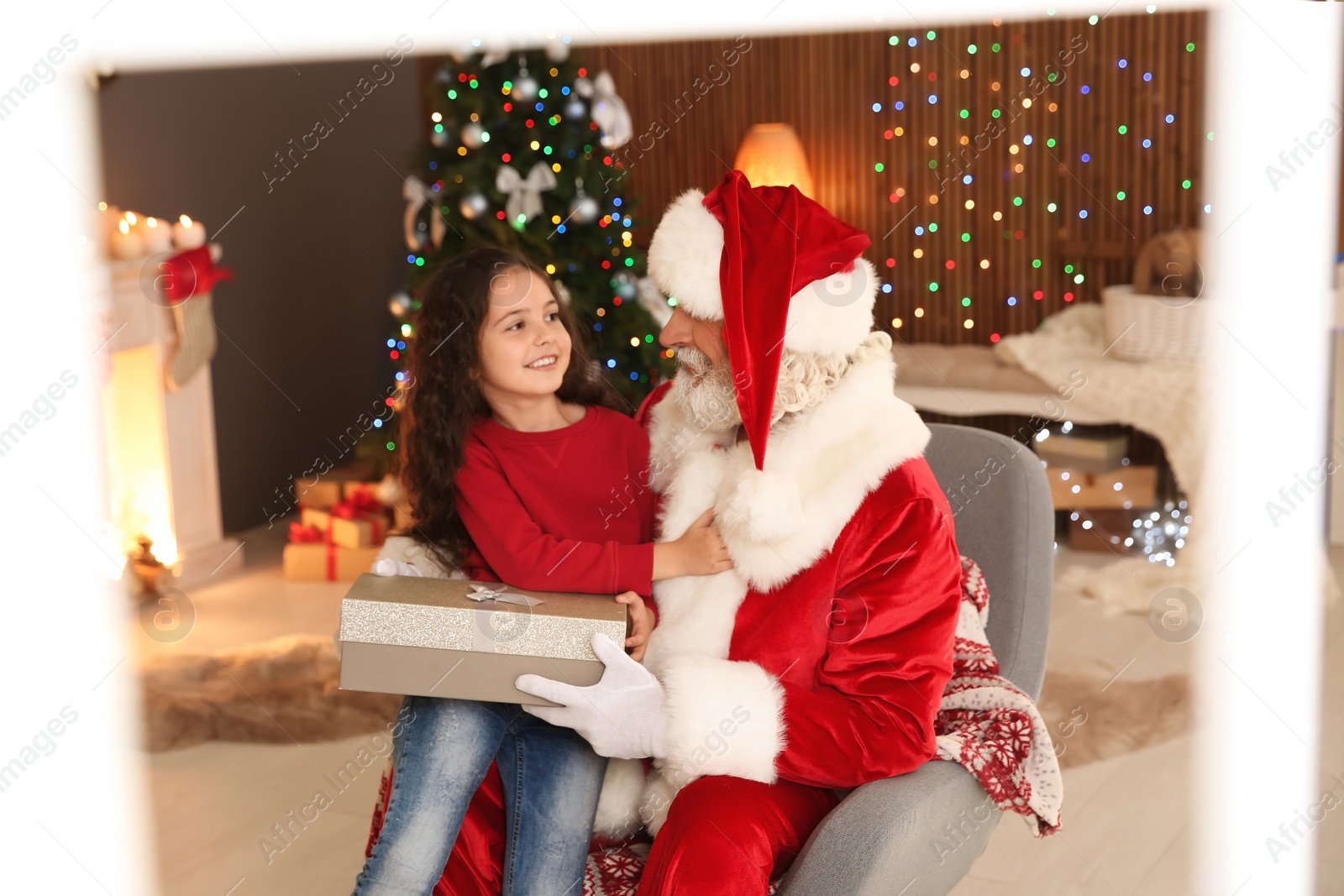 Photo of Little child with Santa Claus and Christmas gift at home, view through window