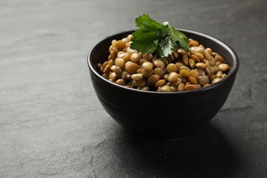 Delicious lentils with parsley in bowl on grey textured table, closeup. Space for text