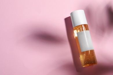 Bottle of cosmetic oil on pink background, top view. Space for text