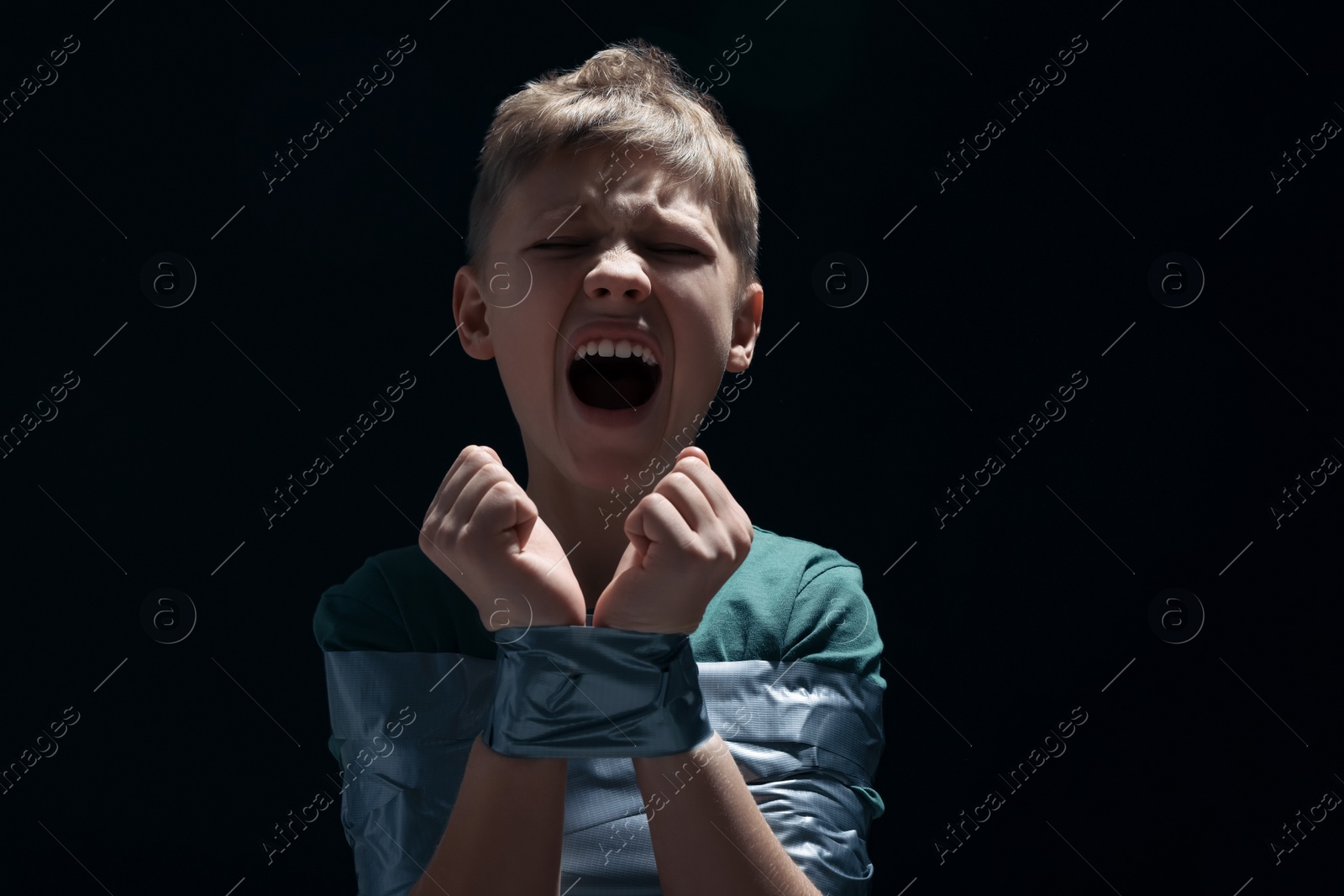 Photo of Scarred little boy tied up and taken hostage on dark background. Space for text