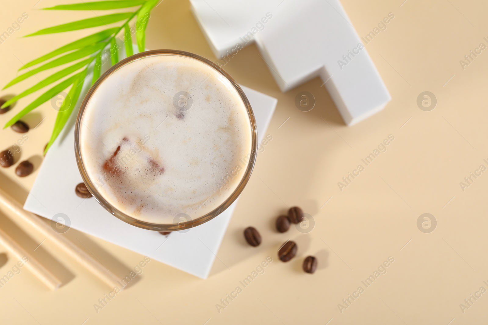 Photo of Refreshing iced coffee with milk in glass and beans on pale yellow table, top view. Space for text