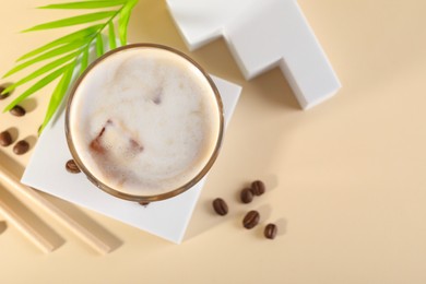 Refreshing iced coffee with milk in glass and beans on pale yellow table, top view. Space for text