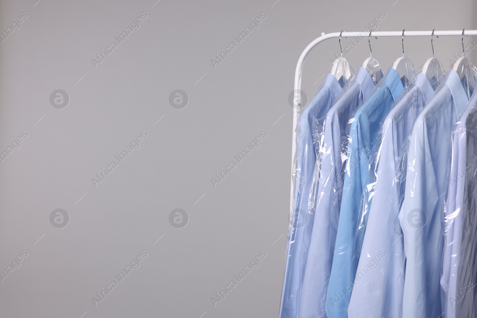 Photo of Dry-cleaning service. Many different clothes in plastic bags hanging on rack against grey background, space for text