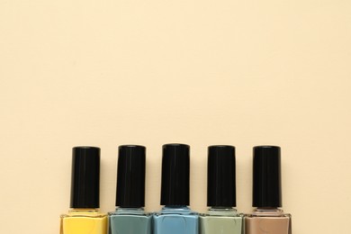 Photo of Bright nail polishes in bottles on beige background, flat lay. Space for text