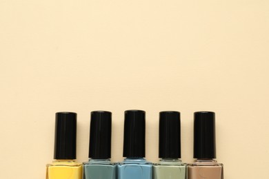 Bright nail polishes in bottles on beige background, flat lay. Space for text