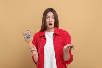 Photo of Emotional woman holding brush with lost hair on beige background. Alopecia problem