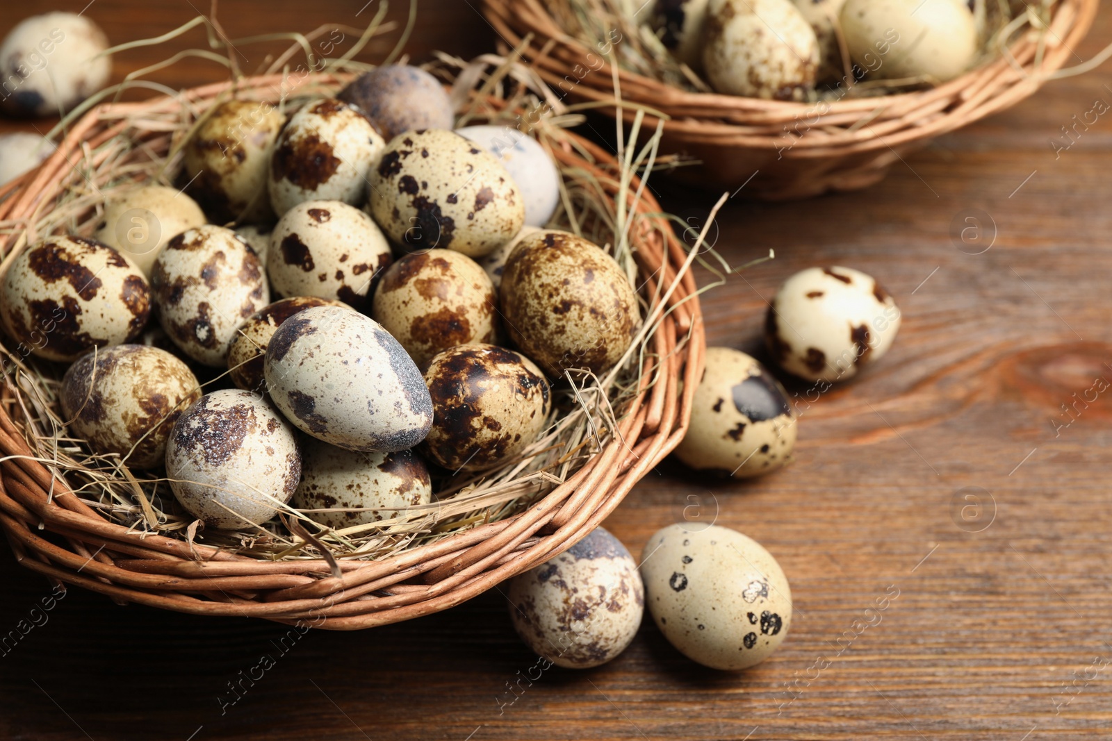 Photo of Wicker bowls, quail eggs and straw on wooden table, closeup. Space for text