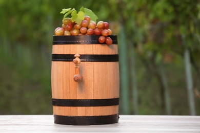 Photo of Wooden wine barrel with ripe grapes on table outdoors