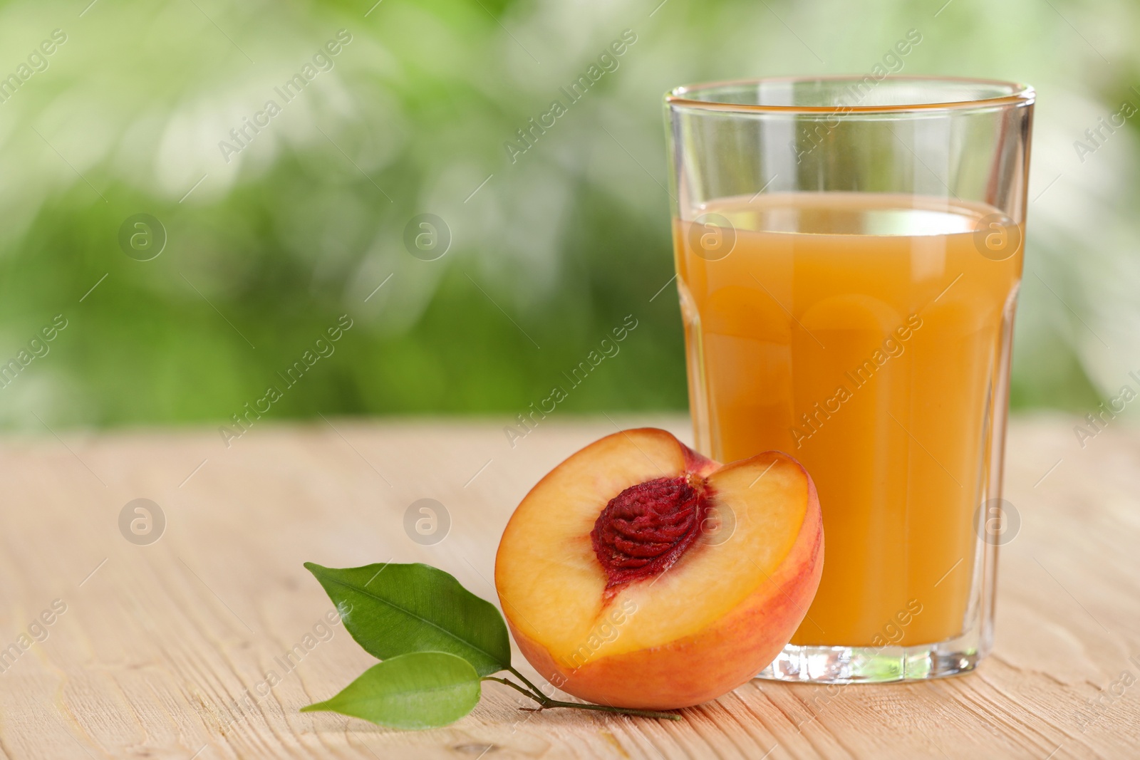 Photo of Tasty peach juice, fresh fruit and green leaves on wooden table outdoors, space for text