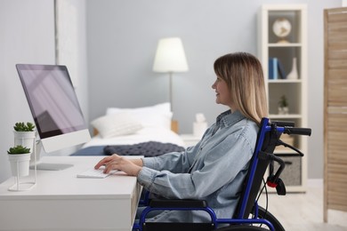 Woman in wheelchair using computer at table in home office
