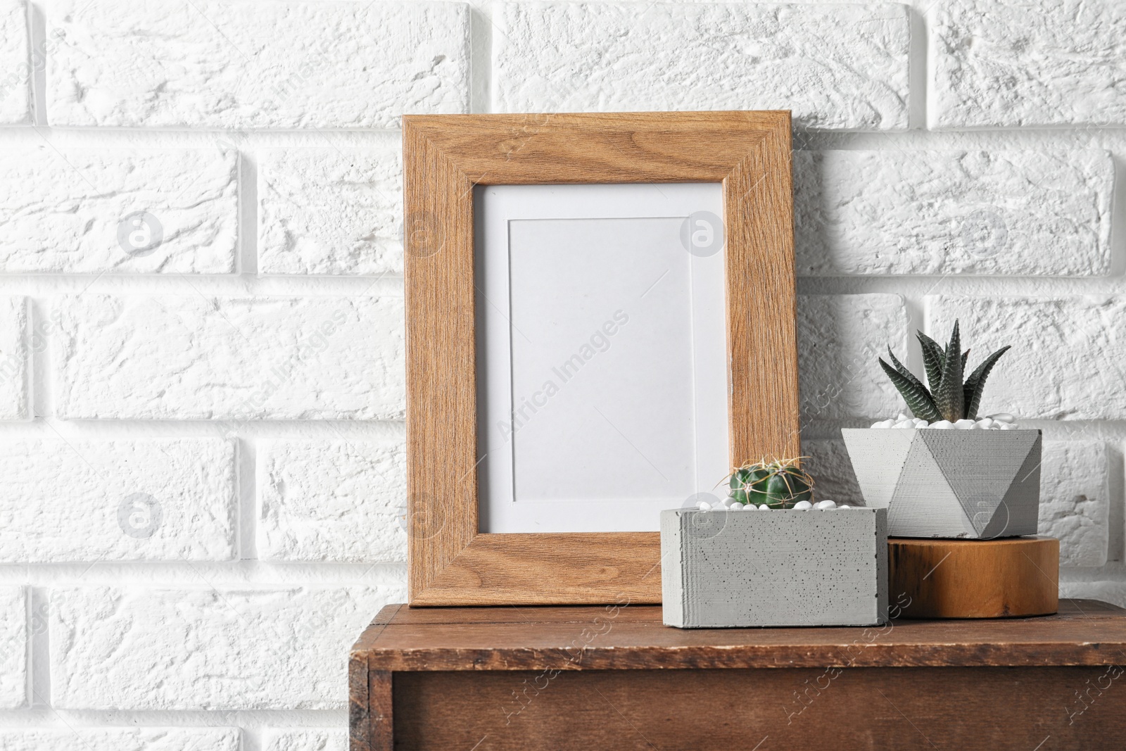 Photo of Blank frame and succulent plants on wooden cabinet near white brick wall, space for design. Home decor